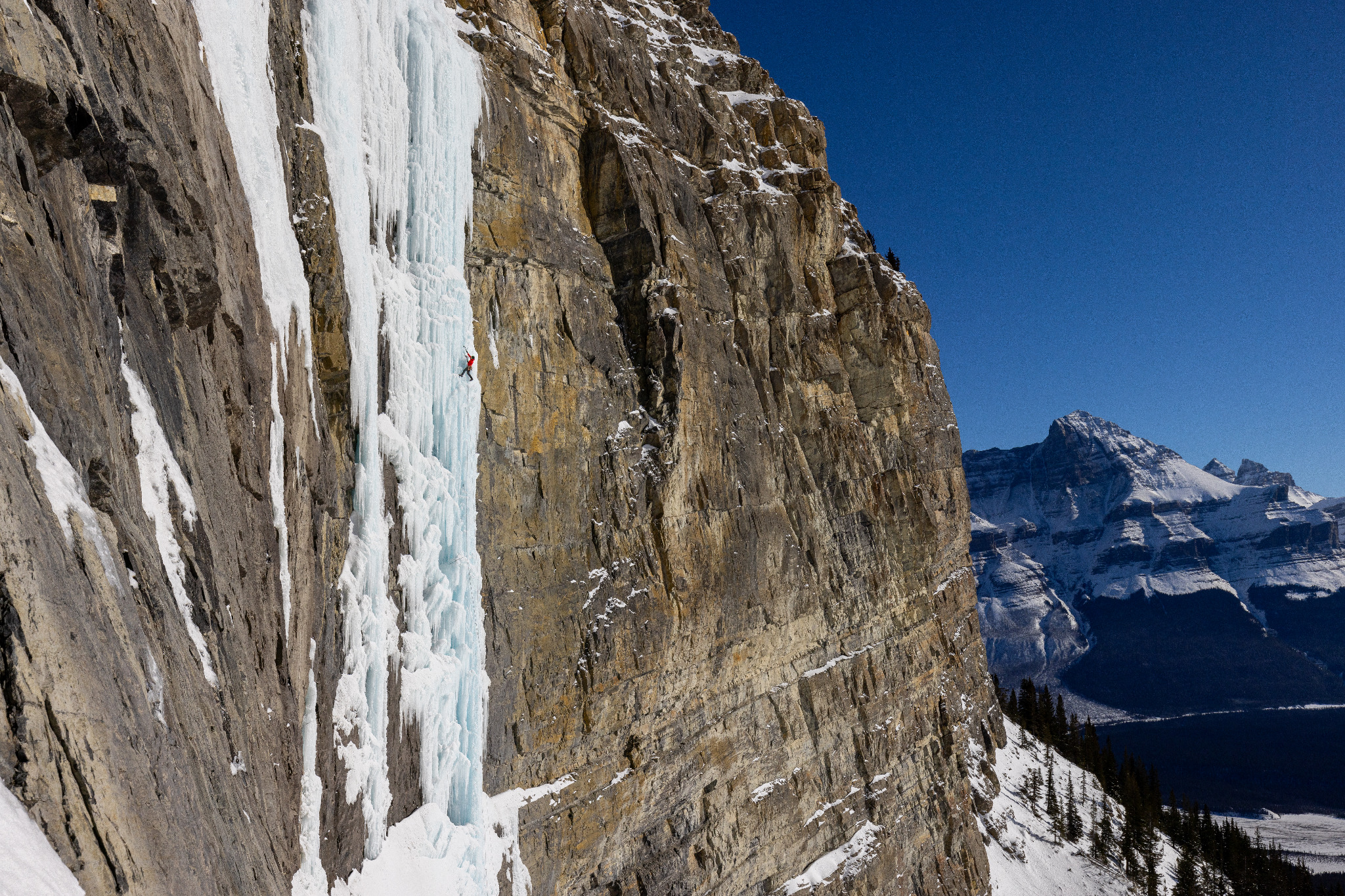 An ice climber on a towering frozen waterfall beneath limestone cliffs in the Canadian Rockies